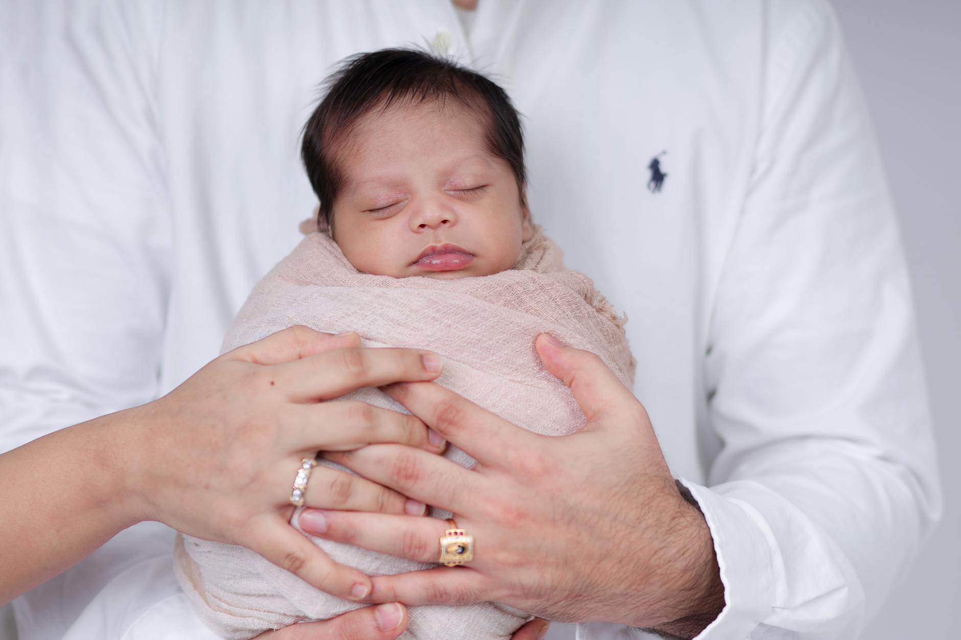 Tender moment of parents cradling their sleeping newborn, wrapped in soft cloth.