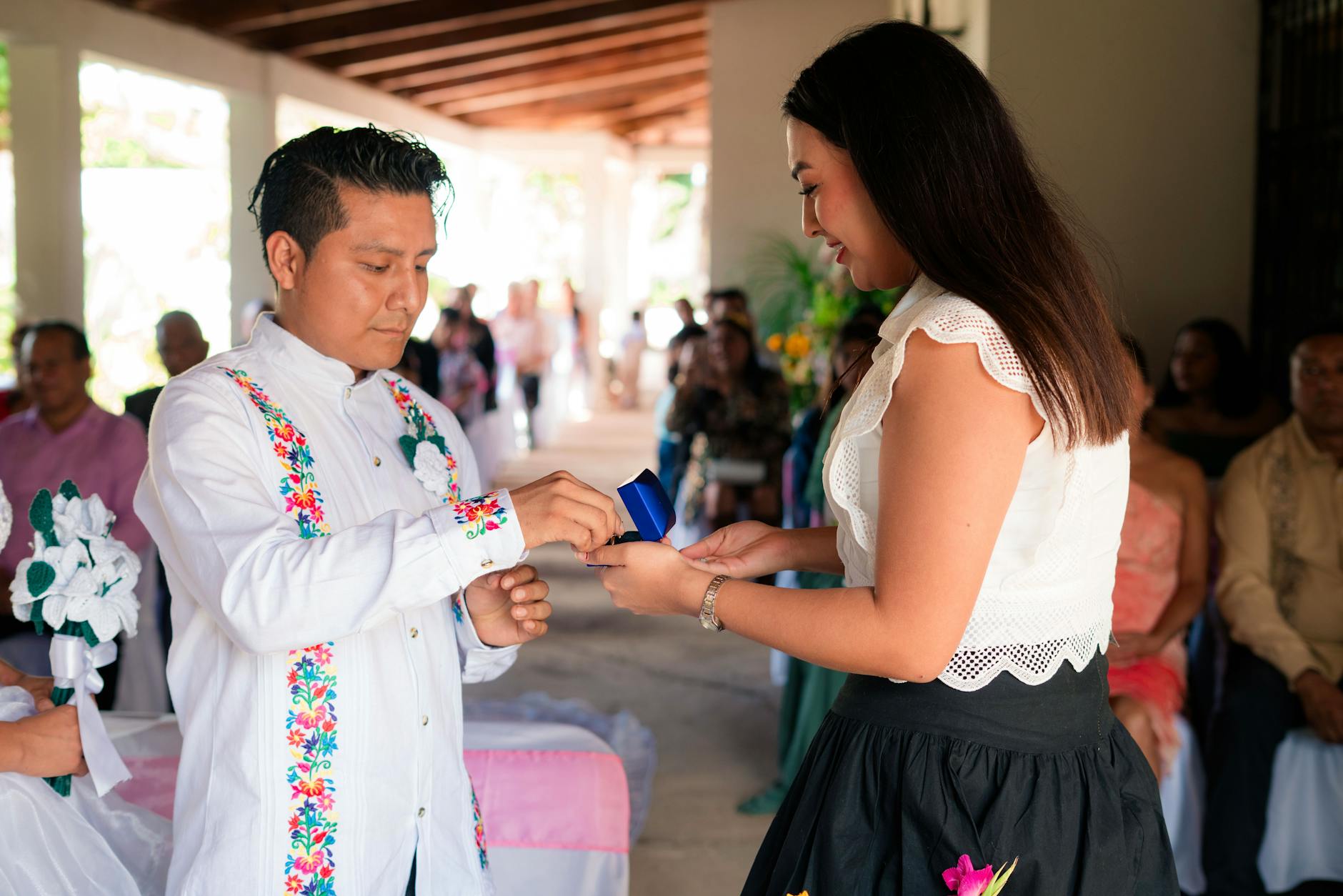 A couple exchanges rings during a vibrant wedding ceremony indoors, surrounded by guests.