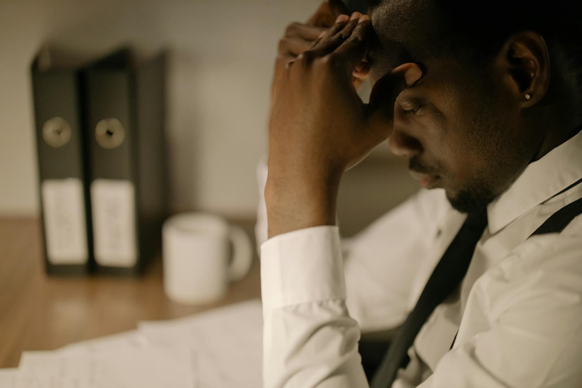 Side view of a stressed businessman in white shirt holding head at a desk with papers.