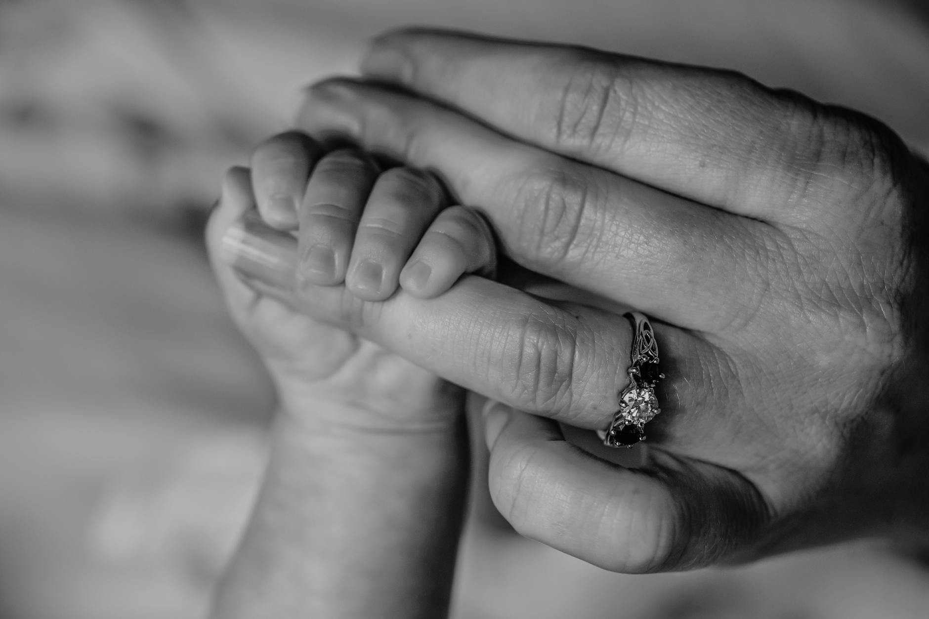 Close-up black and white photo of baby hand holding mother's finger with love.